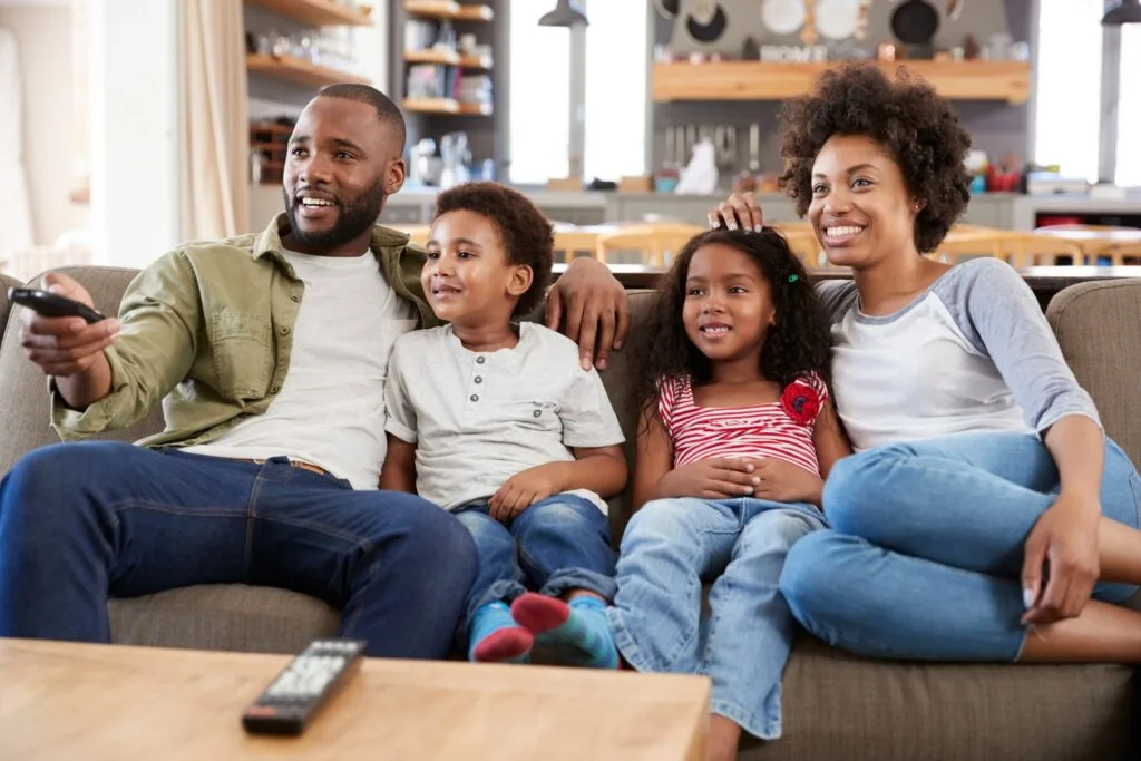 Family Sitting On Sofa In Open Plan Lounge Watching Television