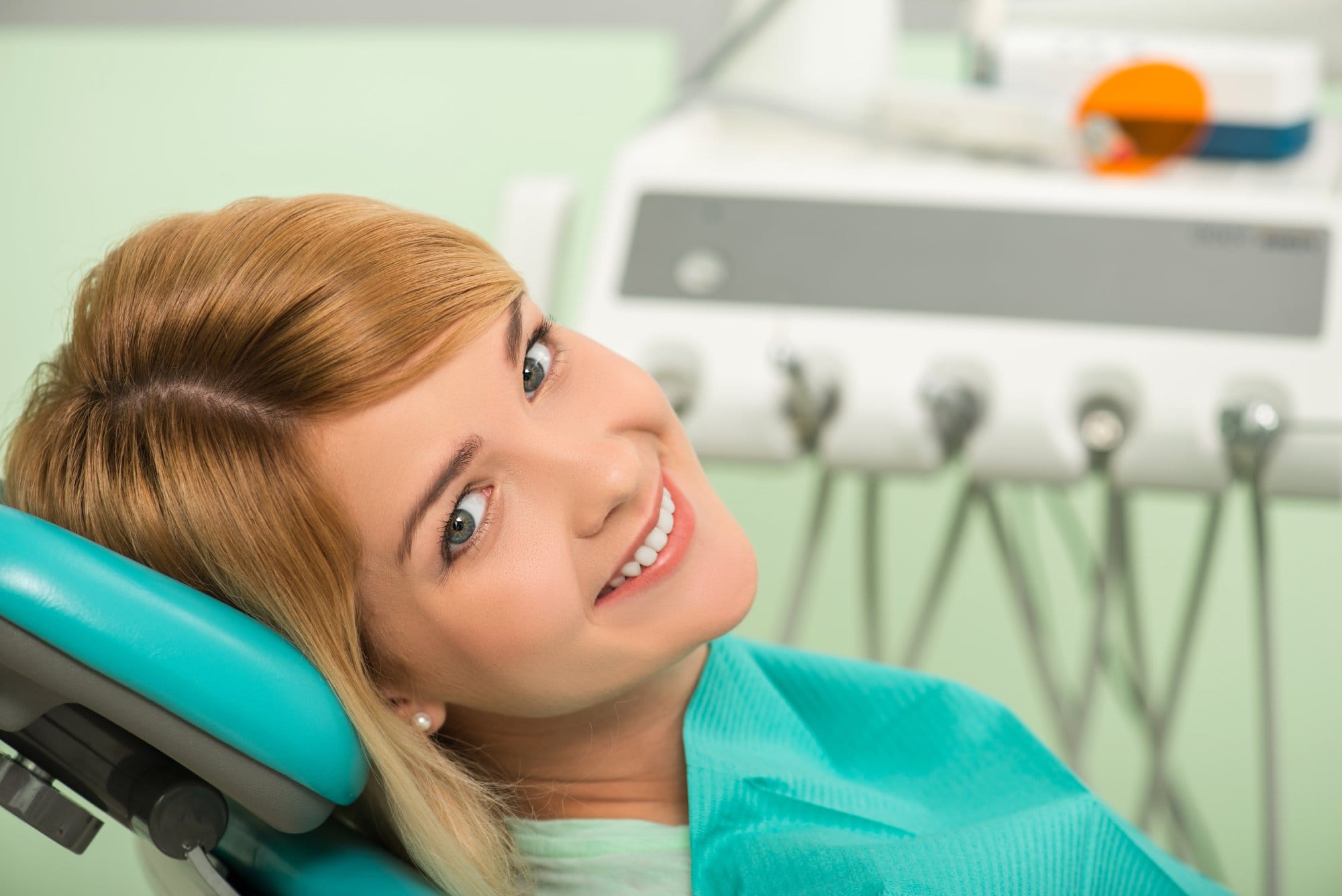 Half-length portrait of nice smiling blonde sitting in the dentist chair looking at us
