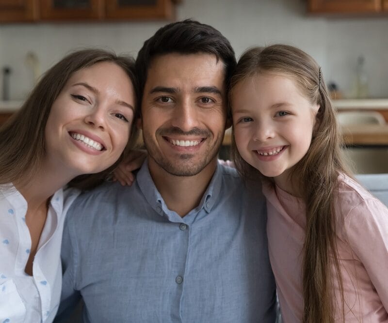 Happy mother, father, and daughter sitting close together on a couch, smiling brightly in a cozy kitchen setting - does laughing gas make you say weird things