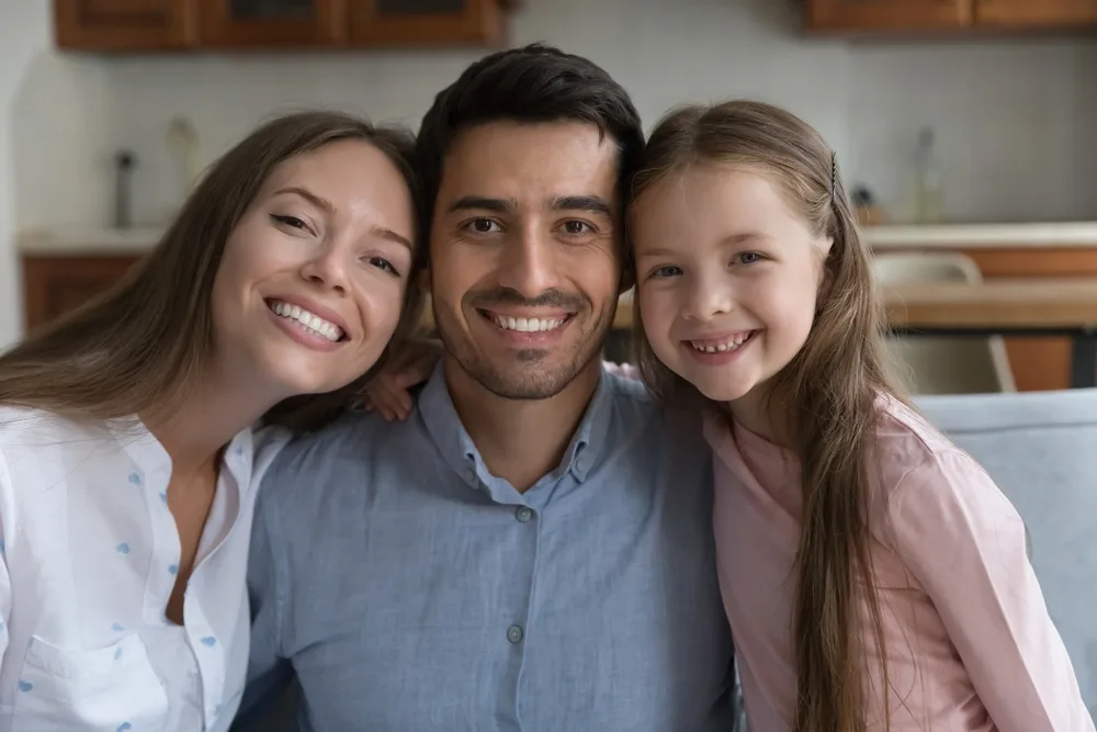 Happy mother, father, and daughter sitting close together on a couch, smiling brightly in a cozy kitchen setting - does laughing gas make you say weird things
